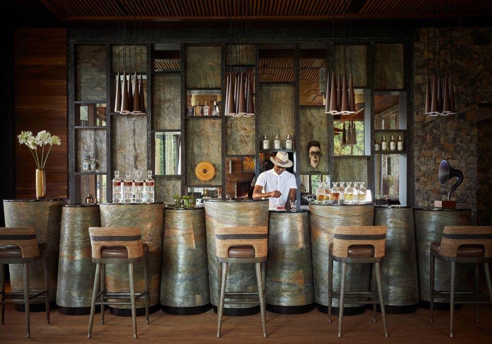 One&Only Gorilla's Nest bar interior with carved columns, African masks, and warm lighting