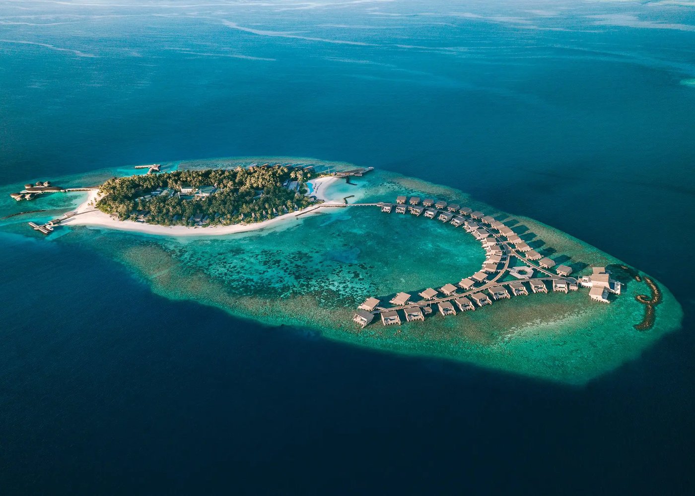 Aerial view of Vommuli Island and the horseshoe overwater villa arc, Dhaalu Atoll